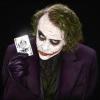 The Joker holding up a playing card, grinning