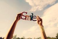 Hands raising a colorful 'Smile' cutout to the sky