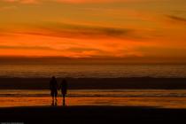 Two silhouettes watching a fiery sunset over the ocean